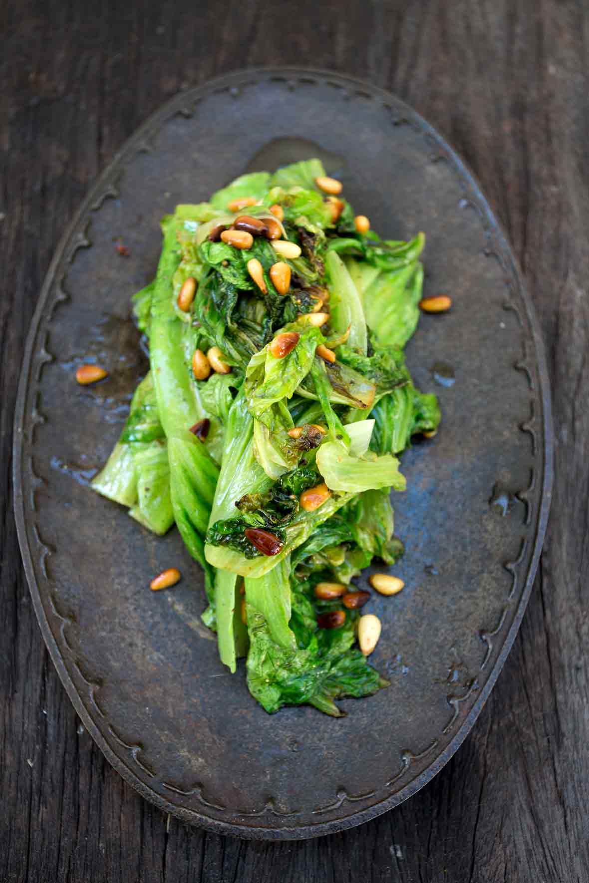 An iron plate with a pile of sautéed romaine lettuce topped with toasted pine nuts