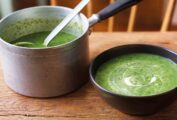 A pot of green watercress soup and a black bowl of soup nearby.