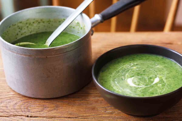 A pot of green watercress soup and a black bowl of soup nearby.