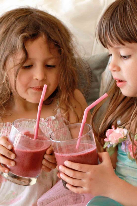 Two small girls holding glasses of red berry smoothies with straws poking out.