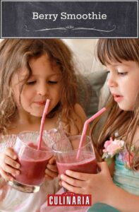 Two small girls holding glasses of red berry smoothies with straws poking out.