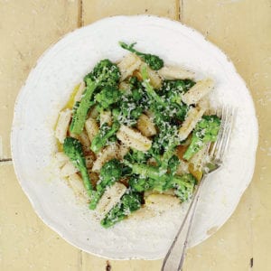 Cavatelli con broccoletti garnished with Parmesan, on a large white pasta dish with a fork.