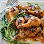Square plate of a pile of grilled sweet and sticky sriracha drumsticks and grilled scallions