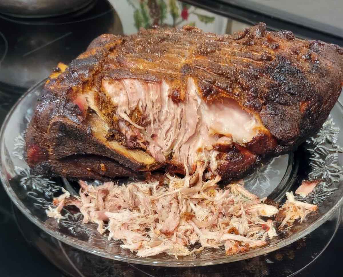 A roast pork butt, partially shredded, on a plate on top of a stove.
