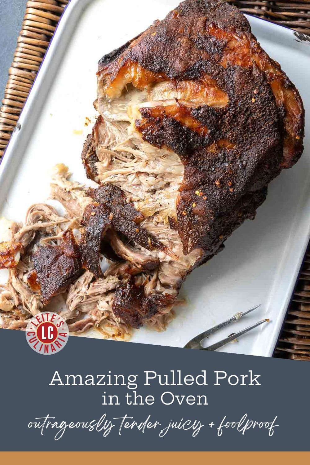 A large piece of roasted pork butt on a white enamel serving tray, shredded and ready to be served with two meat forks.