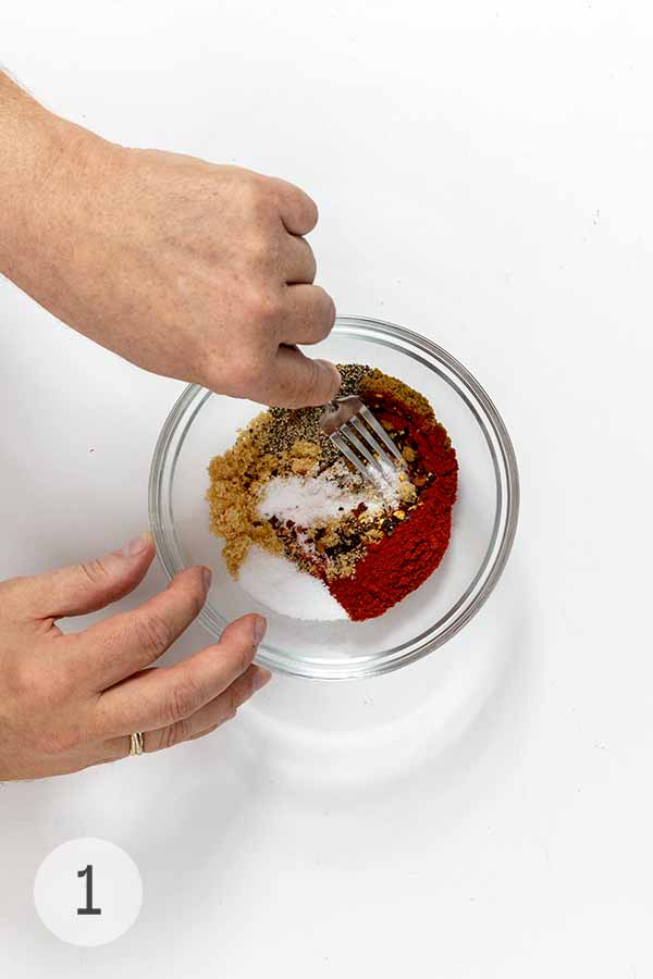 A man's hands mixing a bowl of spices for a oven-roasted pork butt.