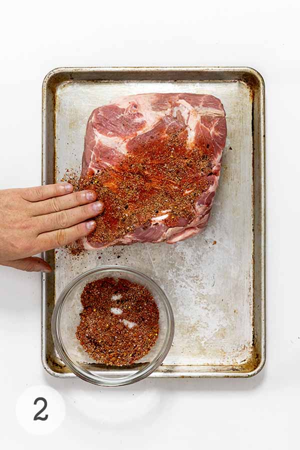 A man's hand rubbing in spice mix into a park butt/pork shoulder.