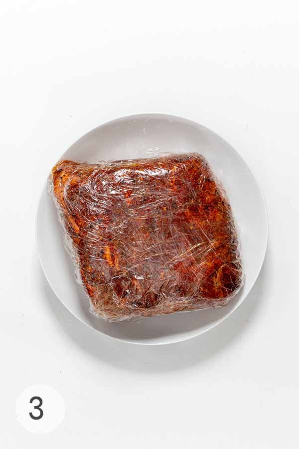 A pork butt wrapped in plastic on a white plate.