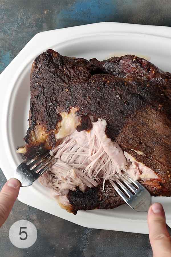 A man's shredding meat for pulled pork with two forks.