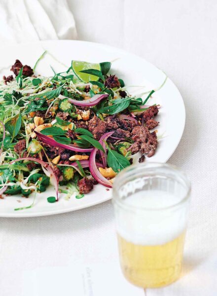 A white plate of larb--salad greens, ground beef, onions, and cashews.