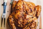 Whole roast chicken with browned lemon slices on the skin all on a cutting board
