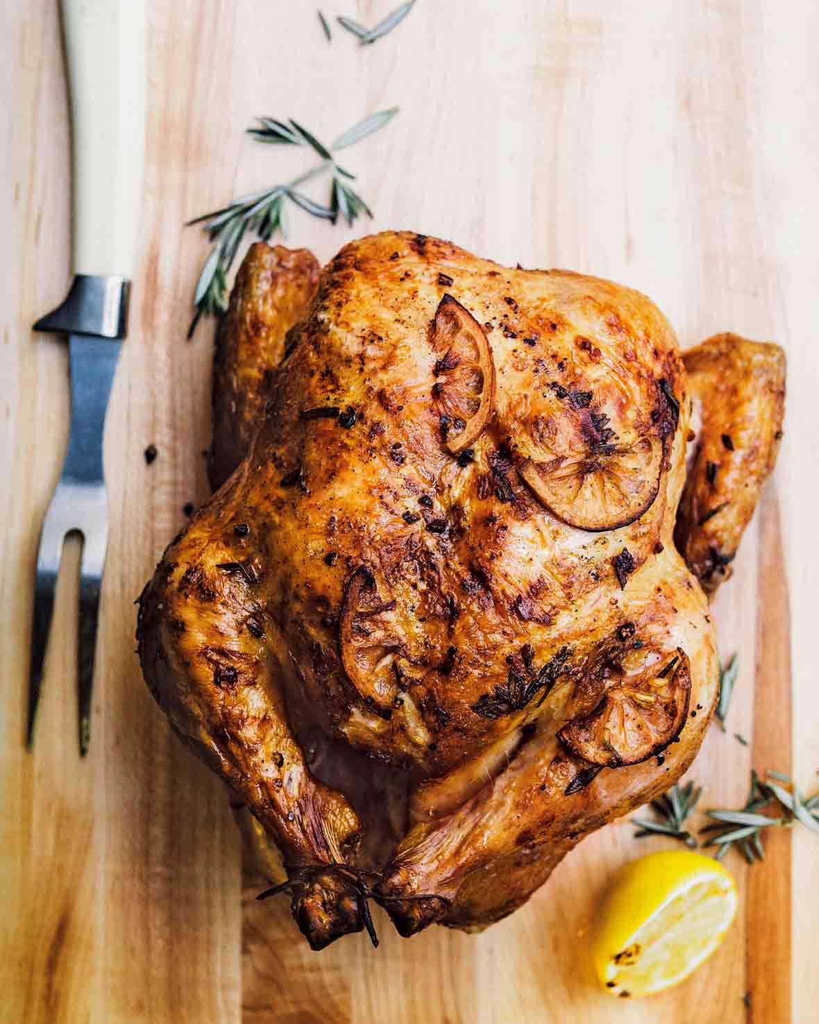 Whole roast chicken with browned lemon slices on the skin all on a cutting board