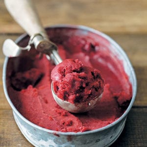 An ice cream scoop with a scoop of easy fruit sorbet resting on top of a container of sorbet.