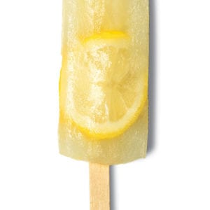 A lemon ginger popsicle with an imbedded lemon slice, lying on a white background.