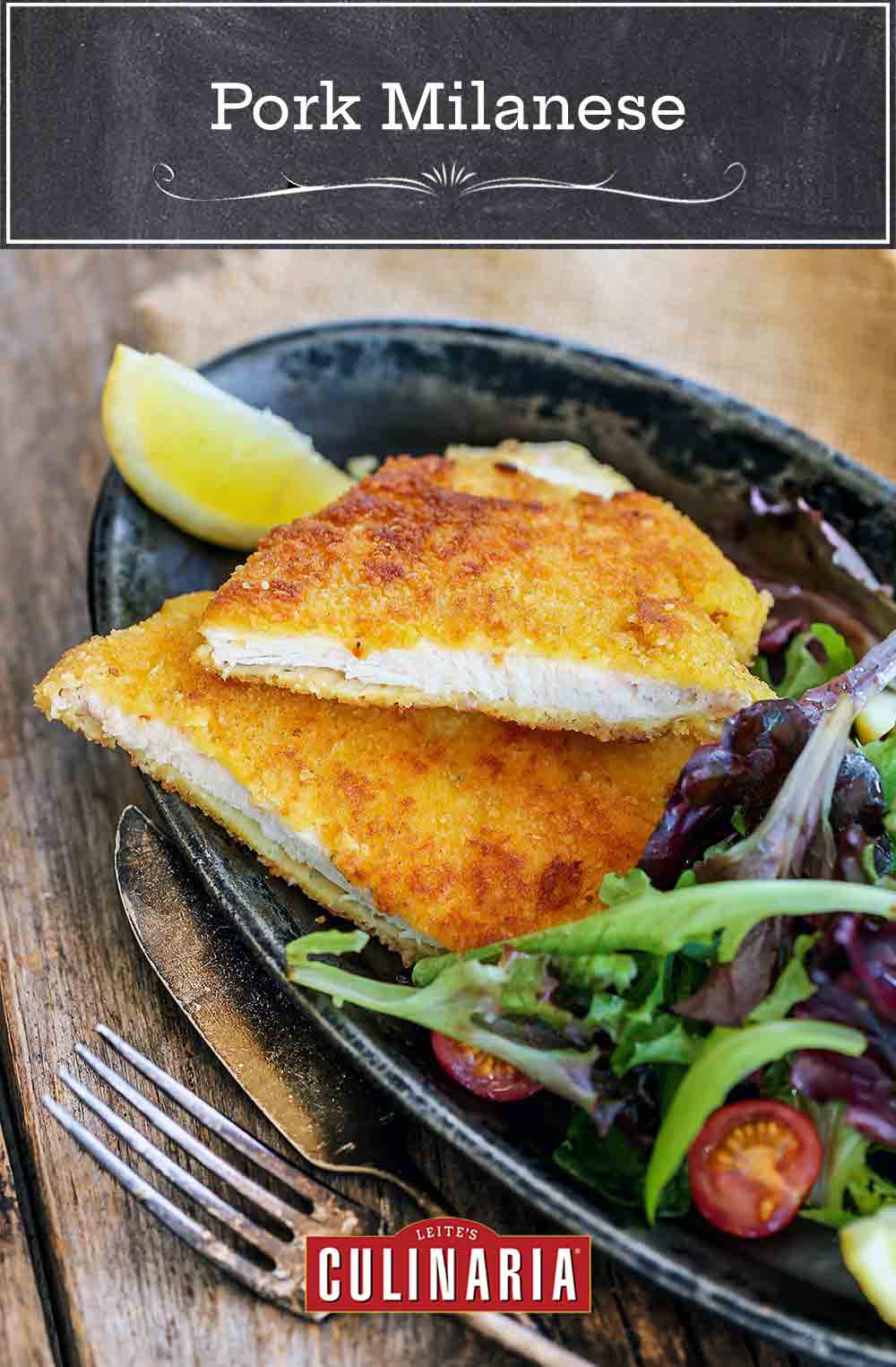 A halved pork Milanese cutlet on a grey oval plate with a lemon wedge and mixed spring greens.