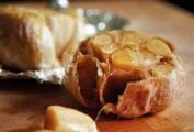 Two heads of roasted garlic--one in foil, one unwrapped--drizzled with oil on a cutting board.