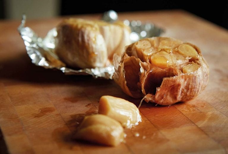Two heads of roasted garlic--one in foil, one unwrapped--drizzled with oil on a cutting board