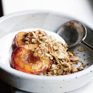 A white bowl of roast peaches topped with an easy granola of oats and almonds, Greek yogurt underneath