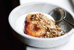 A white bowl of roast peaches topped with an easy granola of oats and almonds, Greek yogurt underneath