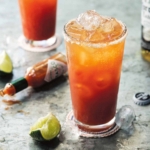A glass filled with Mexican blood Mary, with limes nearby.