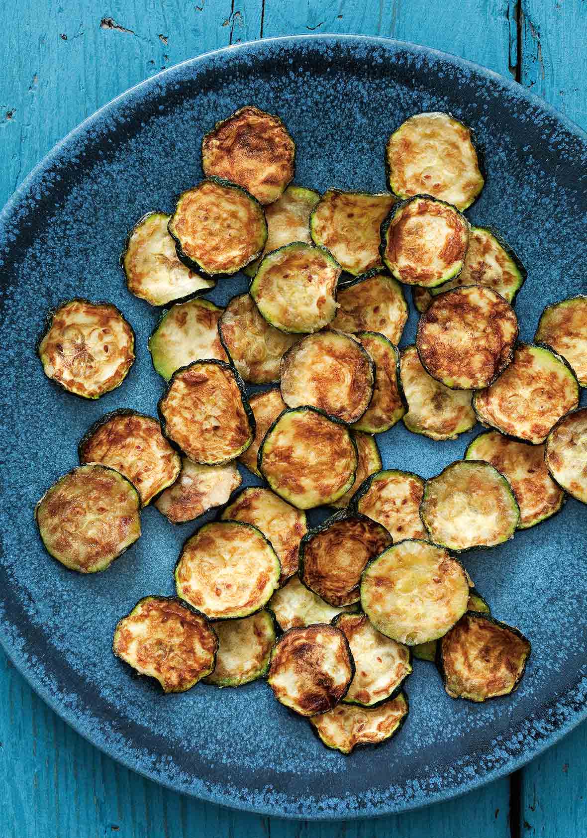 A blue plate filled with slices of zucchini crisps.
