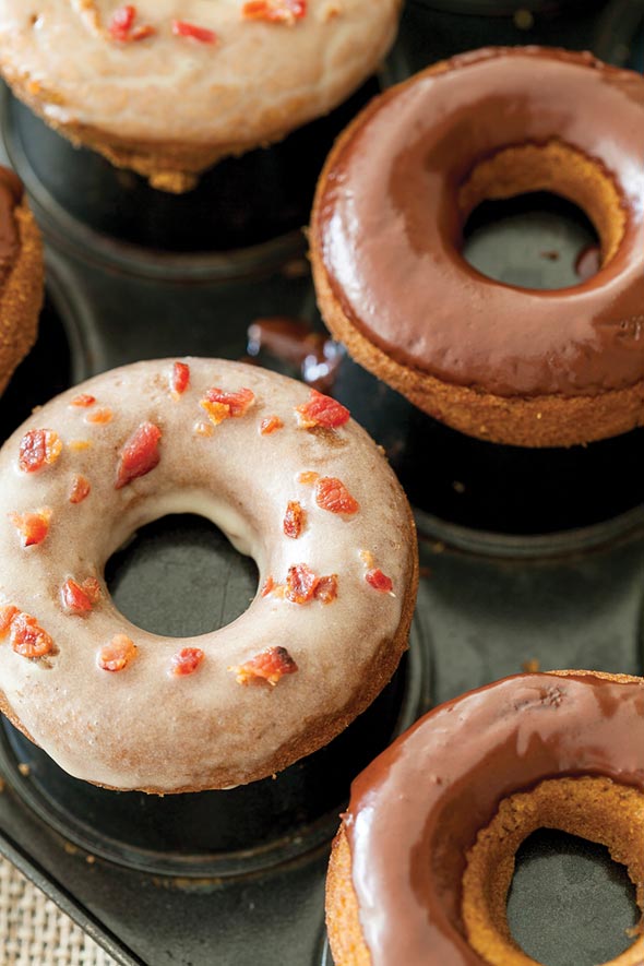 Four baked pumpkin donuts on a donut tray, two coated with dark chocolate frosting and two coated with maple-bacon glaze.