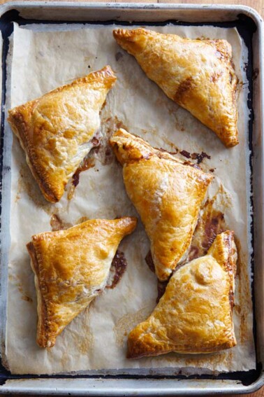 Five pear turnovers on a piece of parchment in a rimmed baking sheet.