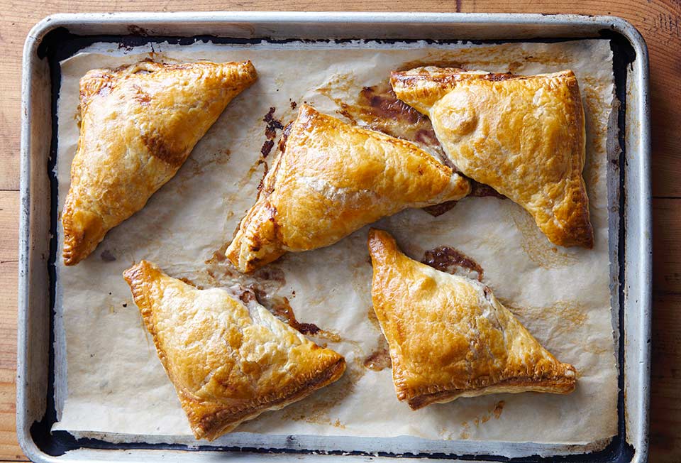 Five pear turnovers on a piece of parchment in a rimmed baking sheet.