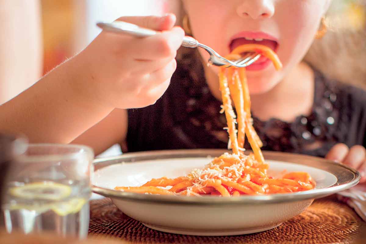Ett barn som äter en skål med kokt pasta med röd sås.