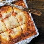 A blue and white square baking dish filled with vegetable lasagna that has been cut into 9 squares with a knife resting on top.