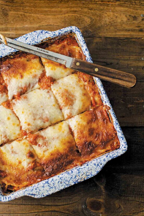 A blue and white square baking dish filled with vegetable lasagna that has been cut into 9 squares with a knife resting on top.