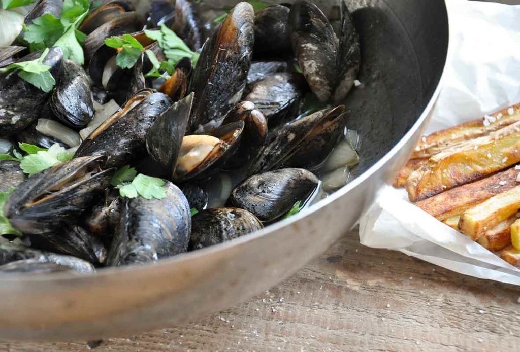 A bowl of apple cider steamed mussels topped with parsley, fries on the side