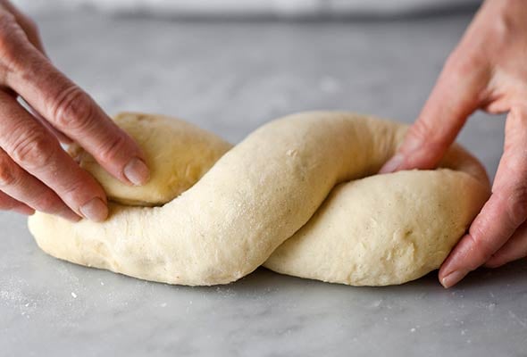 Two hands shaping yeasted sour ream dough into a babka.