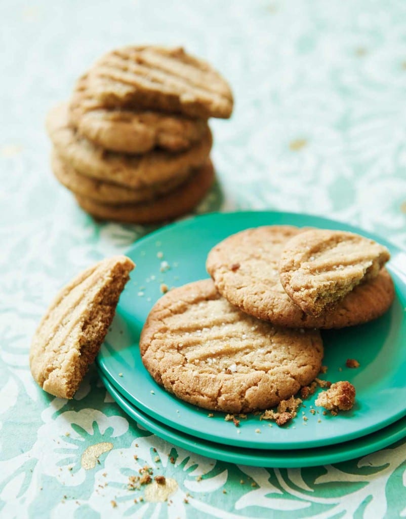 Two and a half bacon fat peanut butter cookies on two stacked green plates with a stack of cookies in the background.