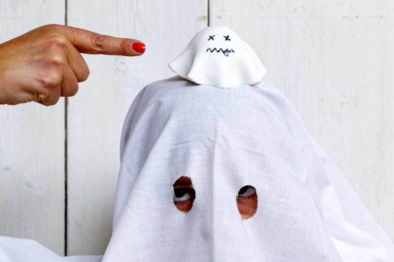 A child dressed as a ghost with a ghost cupcake on their head.