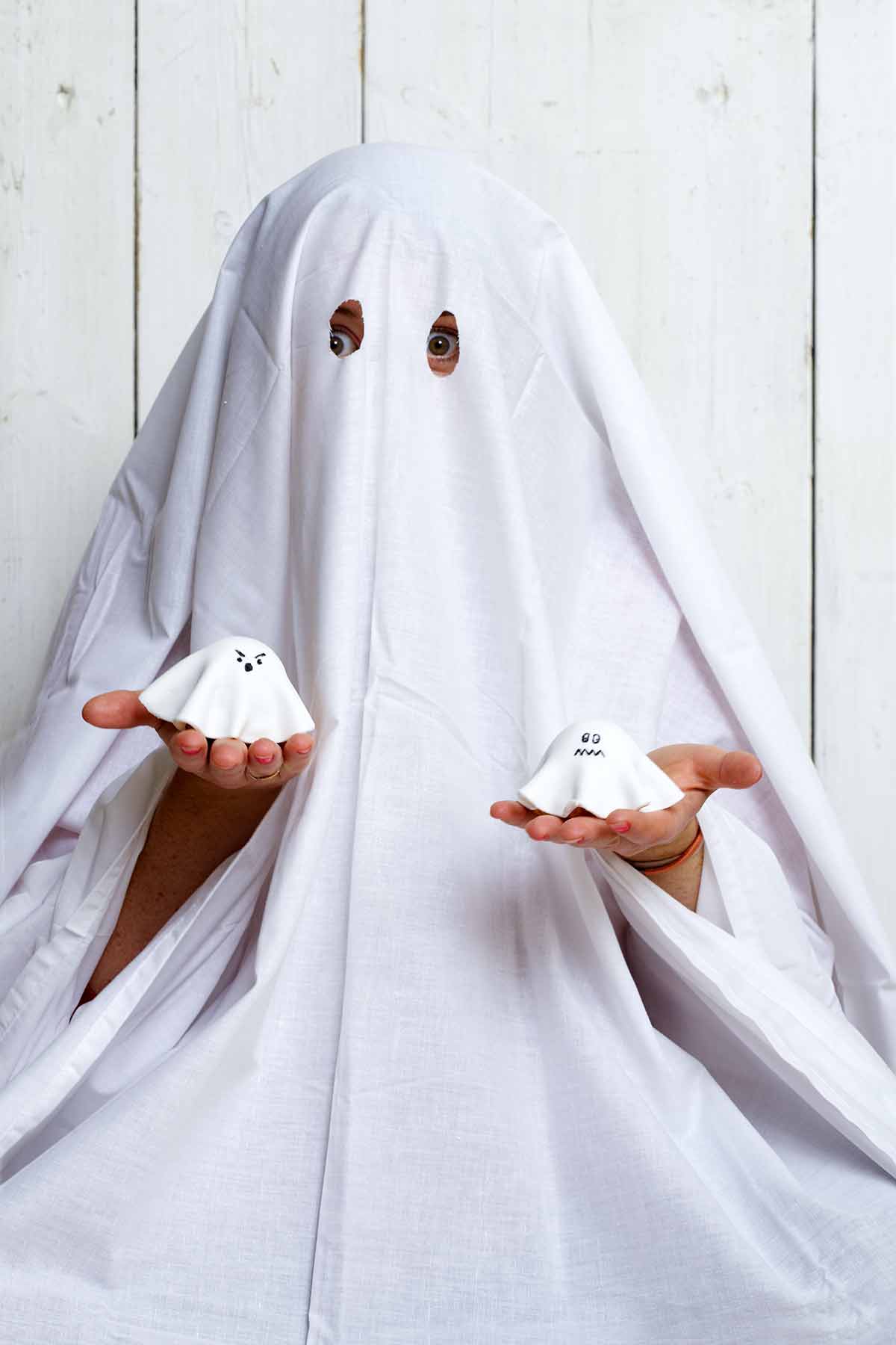 A child dressed as a ghost, holding a ghost cupcake in each hand.