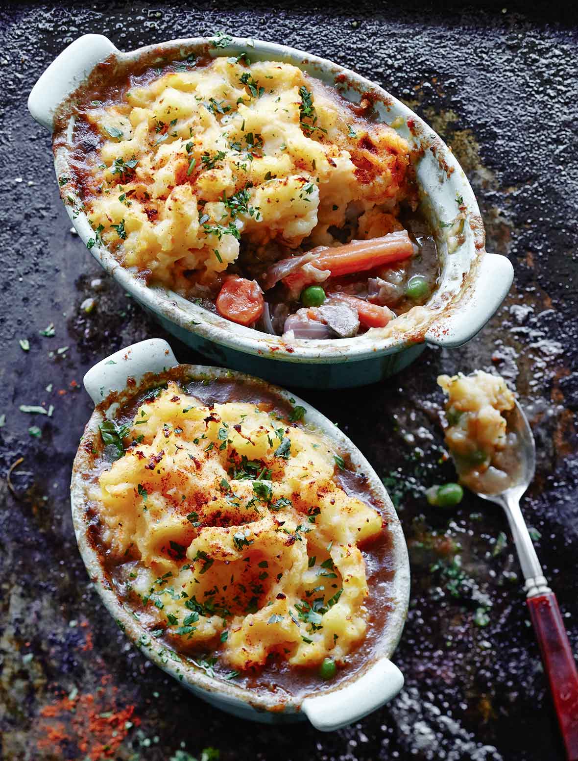 Two oval dishes filled with lamb shank shepherd's pie and a spoon resting beside them.