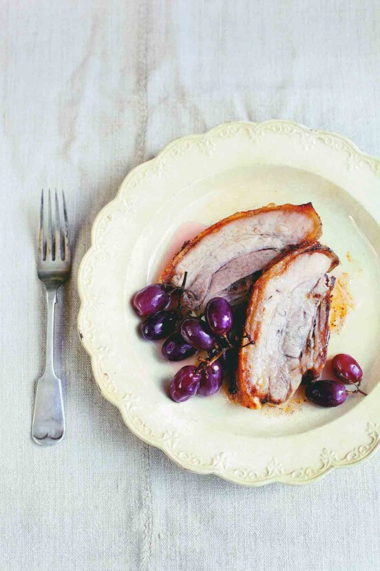 A decorative plate with two slices of roast pork and three bunches of pickled grapes.