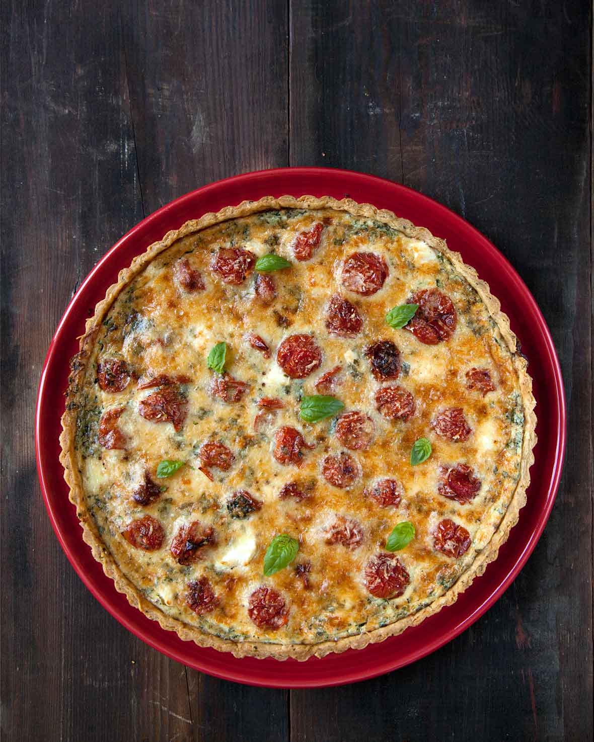 A cooked cherry tomato tart with a herbed crust on a red plate.