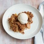 A piece of apple crumble topped with vanilla ice cream in a white bowl.