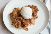 A piece of apple crumble topped with vanilla ice cream in a white bowl.