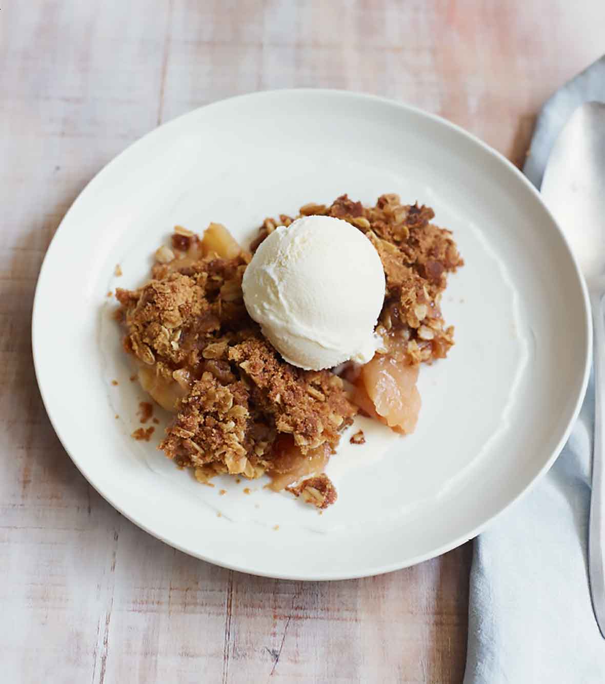 A piece of apple crumble topped with vanilla ice cream in a white bowl.