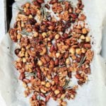 A layer of assorted nuts and rosemary sprigs on a sheet of parchment paper resting in a sheet pan