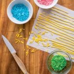 Parchment paper with long lines of yellow homemade sprinkles, plus bowls of green, blue, and pink sprinkles