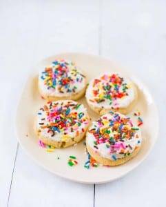 Four sugar cookies topped with frosting and sprinkles on a white plate.
