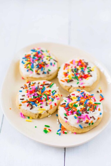 Four sugar cookies topped with frosting and sprinkles on a white plate.