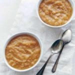 Two bowls of slow cooker applesauce with two spoons nearby