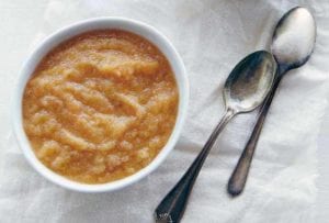 A bowl of slow cooker applesauce with two spoons nearby
