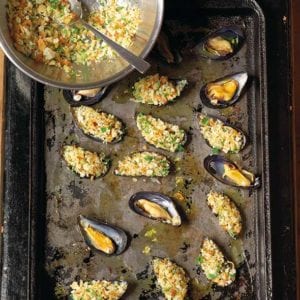 A rimmed baking sheet with stuffed broiled mussels and a bowl of filling on the side