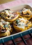 A casserole dish with four halves of roasted winter squash filled with cheese-topped stuffing